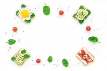 Breakfast with sandwiches, avocado, cucumber, spinach, tomato, bacon, soft cheese on white background. Top view, flat lay