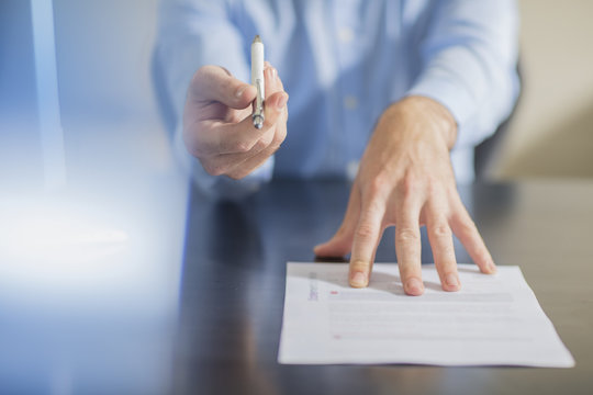 Person sitting at office desk presenting pen and contract