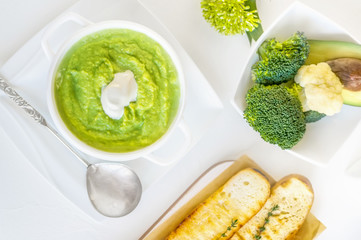 Cream soup of broccoli, avocado and cauliflower with whipped cream on a wooden table. The view from the top.