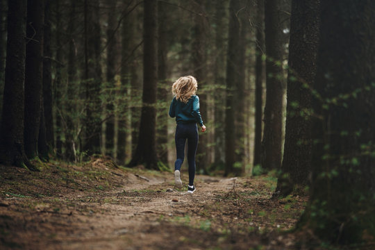 Young fitness woman running in the forest trail