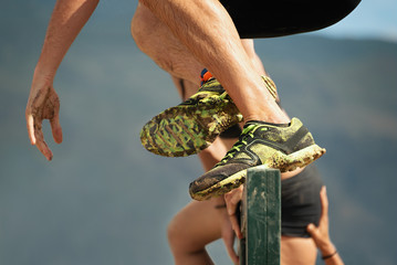 Mud race runners,participants jumps over obstacles,in the background help the woman to overcome the obstacle