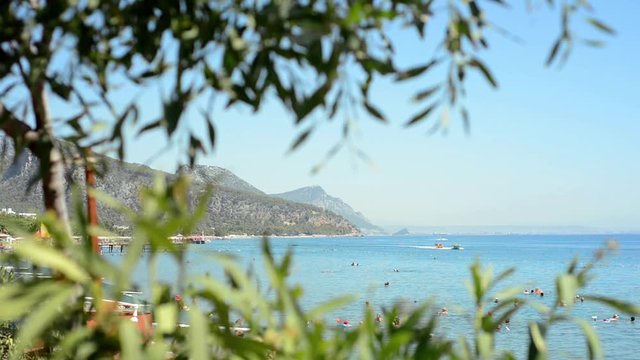Turkey - August 2017: Tropical summer landscape with people on beach, mountains and blue sky through the out of focuse branches