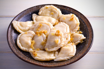 Pierogi or pyrohy, varenyky, vareniki, dumplings served with caramelized salted onion in bowl on wooden table. horizontal