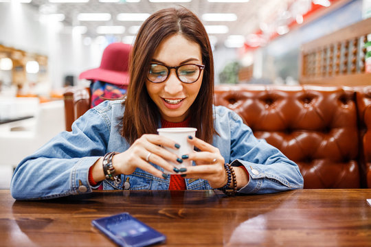Portrait of young beautiful hipster woman sitting in a cafe indoor drinking coffee from a disposable cup