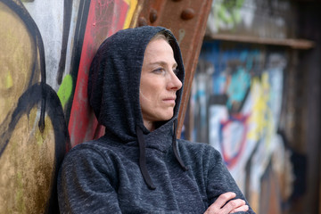 Woman in a hoodie leaning against graffiti
