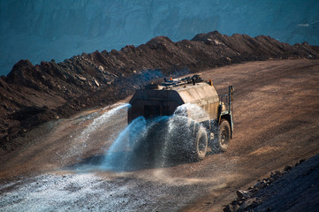 Heavy truck pours the road with water in the iron ore quarry. Dust removal, protection of the...