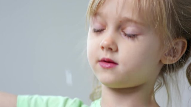 Close up face of adorable little girl with wavy golden hair and two ponytails blowing soap bubbles with bubble wand
