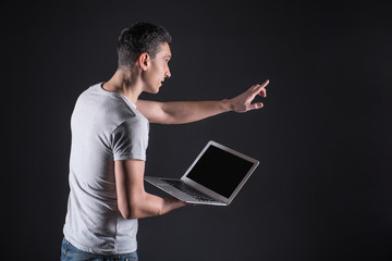 New technology. Smart nice pleasant man holding his laptop and touching the sensory screen while working with new technology