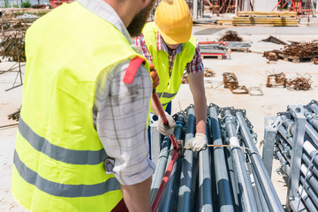 Two efficient blue-collar employees preparing supplies before building a metallic scaffolding while...