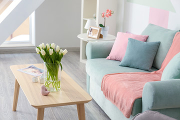 Wooden table with bouquet of tulips near sofa in living room