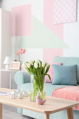 Wooden table with bouquet of tulips near sofa in living room