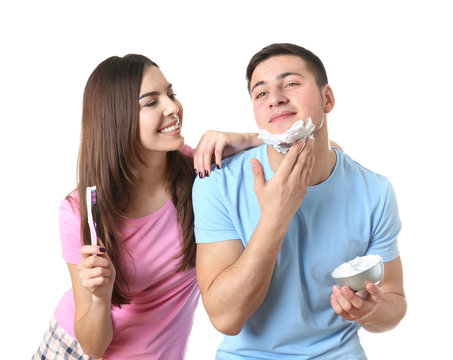 Young man shaving and his girlfriend cleaning teeth on white background