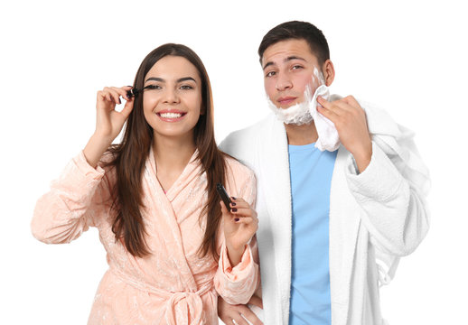 Young man with shaving foam and his girlfriend applying mascara on white background