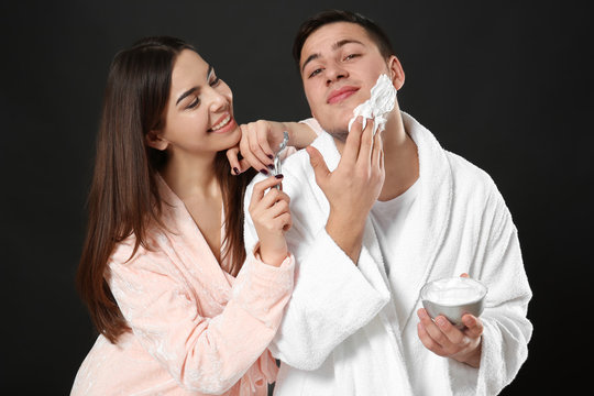Young woman helping her boyfriend shaving on dark background