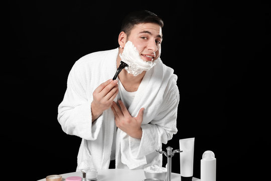 Young man shaving on dark background