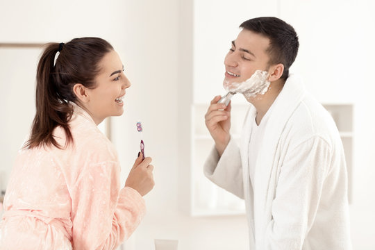 Young man shaving while his girlfriend having fun in bathroom