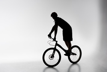 Fototapeta na wymiar silhouette of trial cyclist in helmet balancing on bicycle on white