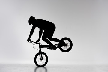 silhouette of trial cyclist performing front wheel stand on white