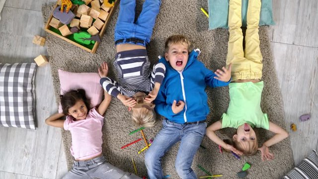 Group of four primary school children lying on carpet on the floor, having fun and making crazy faces, top view