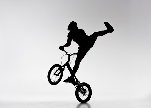 silhouette of trial biker performing stunt on bicycle on white