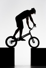 silhouette of trial cyclist balancing on two stands on white