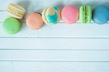 A row of multicolored macaroons or macaron on a white wooden background close-up, almond cookies on a table. Top view, copy space.