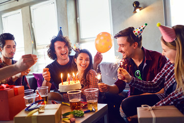 Friends with cake with candles celebrating birthday at a party in room.