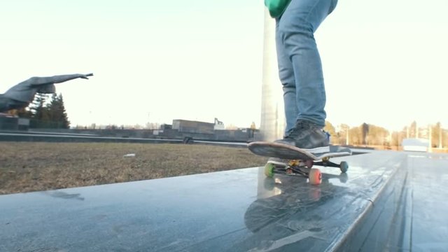 Skateboarder legs on his board on the ramp at sunset