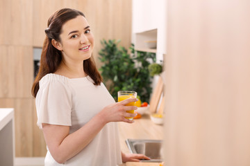 Vitamin C. Happy enthusiastic woman gazing at camera while holding glass of orange juice