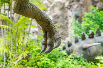 Close up shot from a Hand, claw of dinosaur (theropod) on green jungle with stegosaurus background.