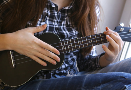 teen girl hands with ukulele guitar in checked shirt and jeans playing close up photo