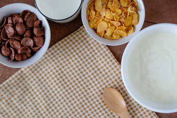 Healthy breakfast with yogurt, Corn cereal, chocolate cereal and milk on wooden background. Diet eating. Top view and copy space