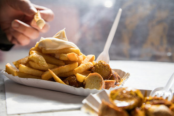 Mann isst Currywurst Pommes Mayo draußen am Wochenmarkt Imbiss