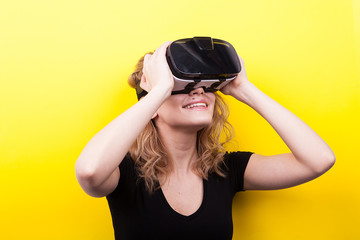 Smilnig woman with a VR headset on enjoying virtual reality experience on yellow background in studio photo