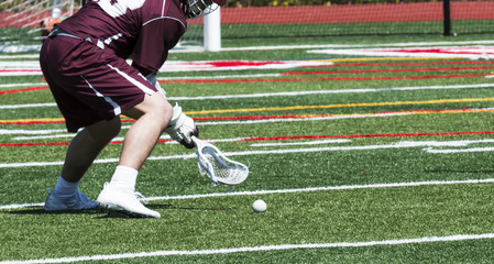 High school lacrosse player scoops up the ball