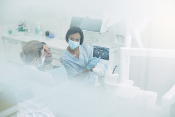 Making a plan. Serious dark-haired dentist holding an image and discussing it with her colleague