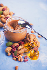 Natural peanut butter with oil in a glass jar and peanuts
