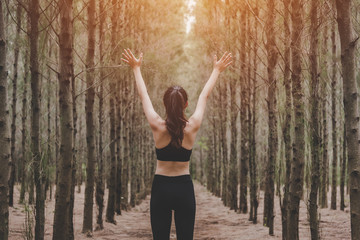 Fototapeta na wymiar Beautiful slim female runner do stretching arms and warm up to running in peaceful forest in morning. Workout and exercise concept. Healthy in nature concept. Pine woods in autumn seasonal theme.
