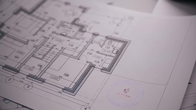 Man's arm puts print stamp on plan of house. Blurred blueprint of house on background