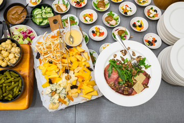 a variety of cheese varieties and meat delicacies next to the table with salads and other fresh sliced