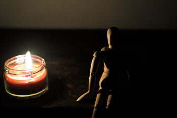 wooden doll on a black background in the light of a candle in a jar