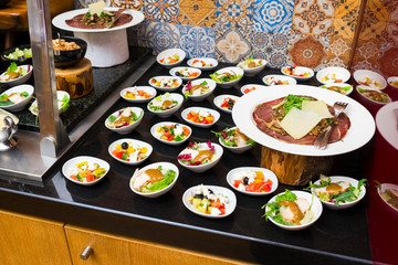 a variety of cheese varieties and meat delicacies next to the table with salads and other fresh sliced