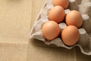Fresh chicken eggs In the thirty box paper and have empty space for egg on cream fabric background.