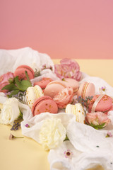 Fototapeta na wymiar Pink and white macaroons cakes with big and small flower buds are decoratively laid on a white fabric on a yellow background
