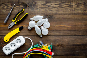 Electrical repair. Bulbs, socket outlet, cabel, screwdriver, pilers on dark wooden background top view copy space