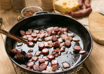 Bavarian sausages are sliced and fried in a frying pan.
