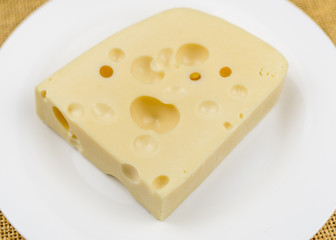 A piece of cheese with holes  on a white plate.