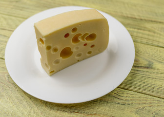 A piece of cheese with holes  on a white plate.