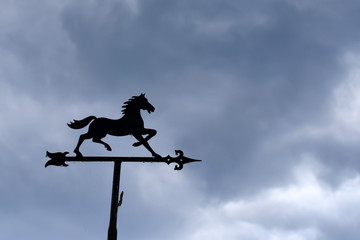 Horse-shaped weather vane against cloudy sky