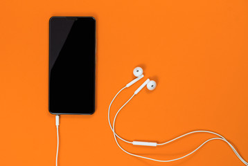 Close-up of smart phone with headphones on a yellow background. (Top view). Listen to music.